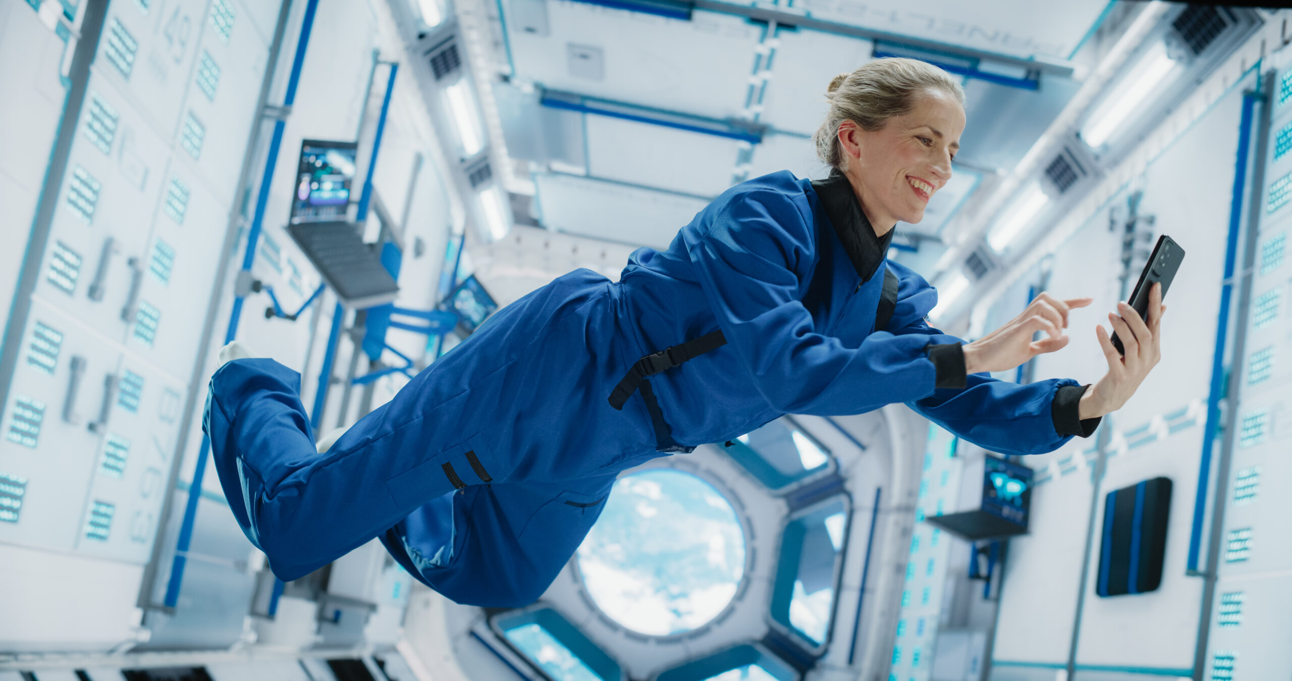 Astronaut Floating in Zero Gravity on Board a Spacecraft. Caucasian Female Having a Video Call with a Family or Friends From Planet Earth. Engineer Using Smartphone in Space Inside Orbiting Spaceship